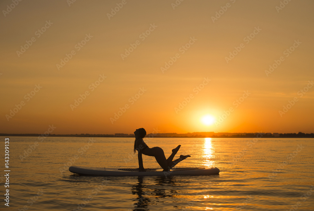 Beautiful young sporty woman is training on the surf desk at sunset time