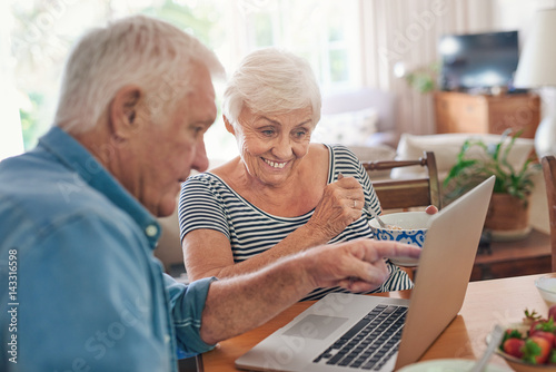 Smiling seniors using a laptop together over breakfast at home