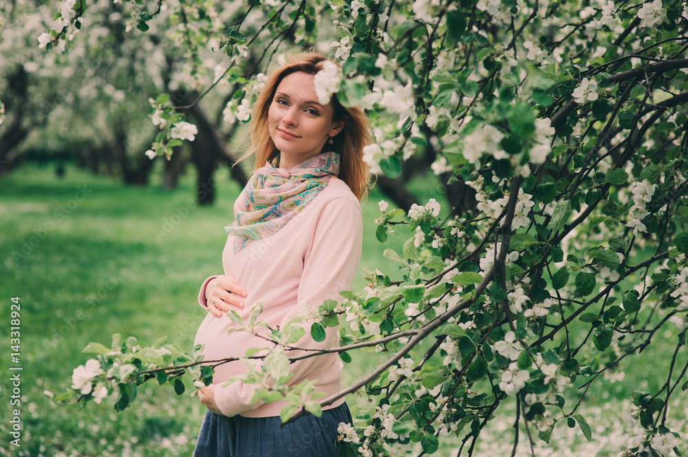 happy pregnant blonde beautiful woman walking outddor in spring park or garden, posing near blooming tree happy pregnant blonde beautiful woman walking outddor in spring park or garden, posing near blooming tree