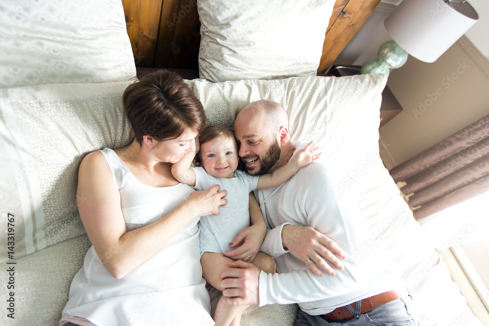beautiful mother and handsome father with baby daughter lying on bedroom