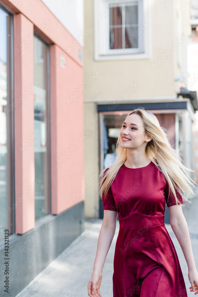 Blonde Frau in rotem Kleid geht in Innenstadt einkaufen