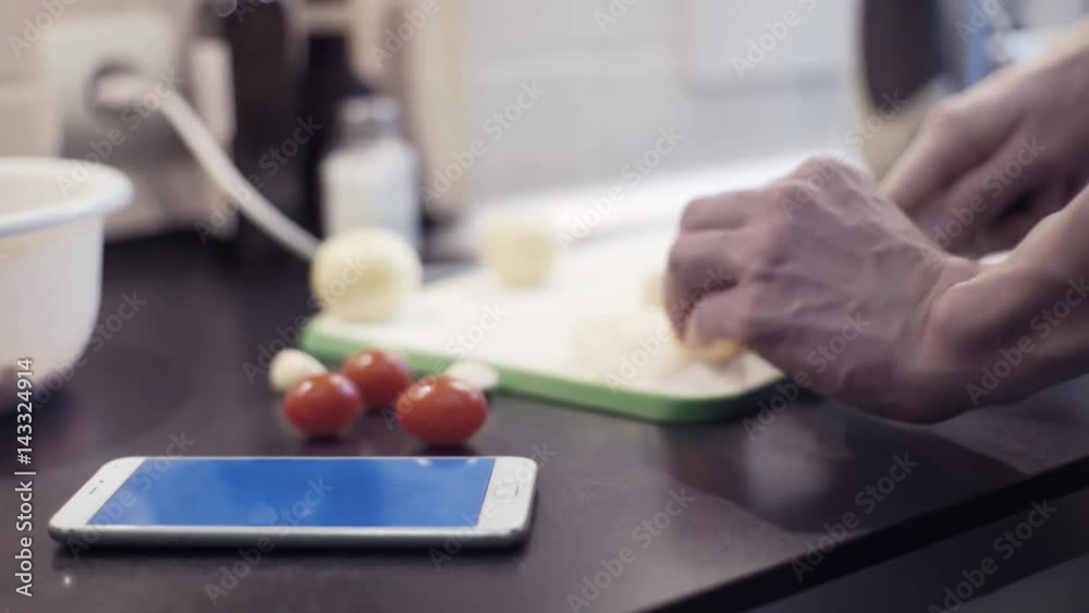 Male hands cutting onion at kitchen preparing vegetable meal using smartphone Male hands cutting onion at kitchen preparing vegetable meal using smartphone