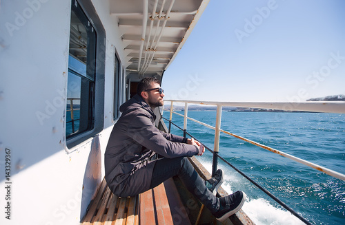 Close up portrait Handsome man in sunglasses on vessel.casual style,happy traveler,grey coat,bearded man,hipster,boat,sea view,looking to a distance,sunny day,attractive,stylish outfit,man's fashion