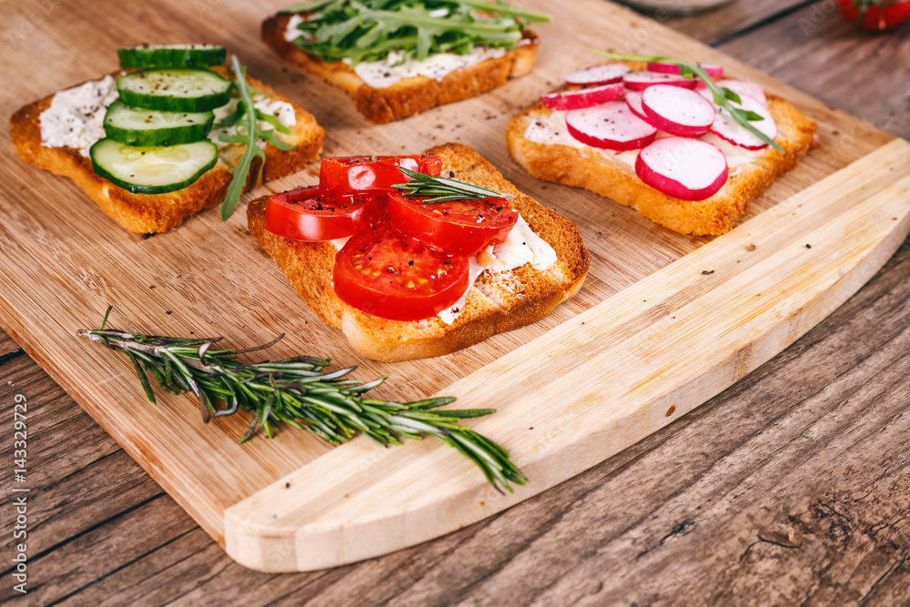 Four sandwiches with fresh vegetables, tomatoes, cucumbers, radish and arugula on a wooden background. Homemade butter and toast. selective focus. Four sandwiches with fresh vegetables, tomatoes, cucumbers, radish and arugula on a wooden background. Homemade butter and toast. selective focus.