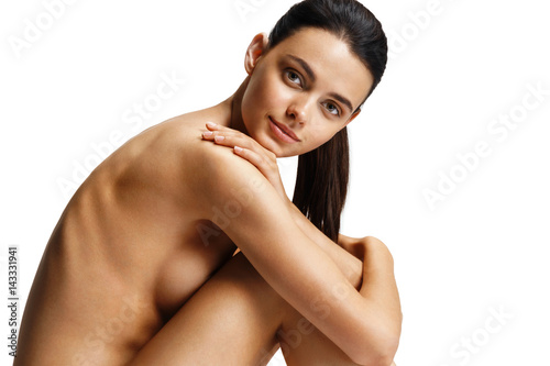 Photo sur Aluminium Beau mannequin nu avec un corps parfait sur fond blanc.  Photo d&#39;une femme assise sur le sol, touche les jambes. Concept de  beauté et de soins de la peau -