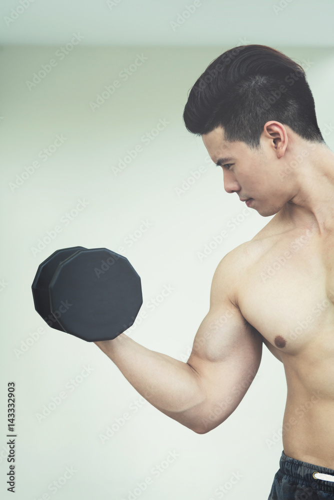 Asian Muscular man lifting dumbbells in gym. copy space.
