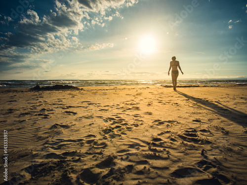 Beautiful girl walking on the beach in bikini with long shadow, France