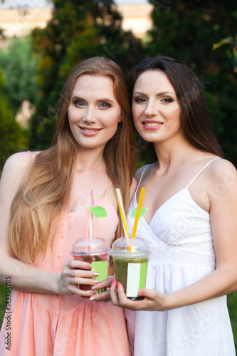 Beautiful young girls in dresses drinking juice in the garden