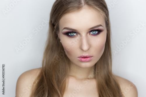 Fashionable portrait of a beautiful sexy girl with crazy hairstyle with bright colored makeup with bared shoulders in the studio on a white background
