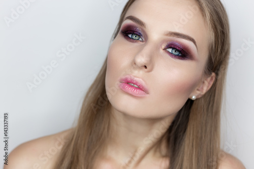 Fashionable portrait of a beautiful sexy girl with crazy hairstyle with bright colored makeup with bared shoulders in the studio on a white background