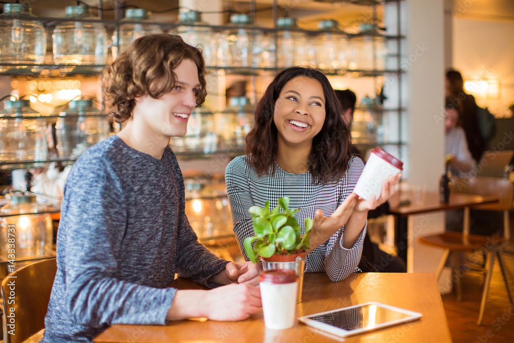 Smiling couple sits in cafe with cups of coffee and the tablet, in time of a break, inside