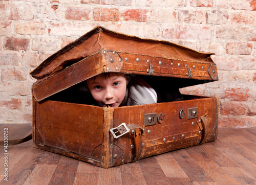 A boy looks out from an old leather suitcase