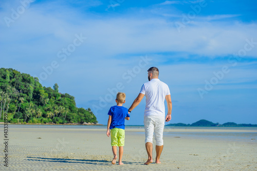 Happy father and son at the tropical beach, laughing and enjoing time together. Back view