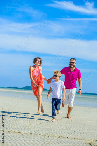 Family of three running and jumping along the tropical beach, laughing and enjoing time together