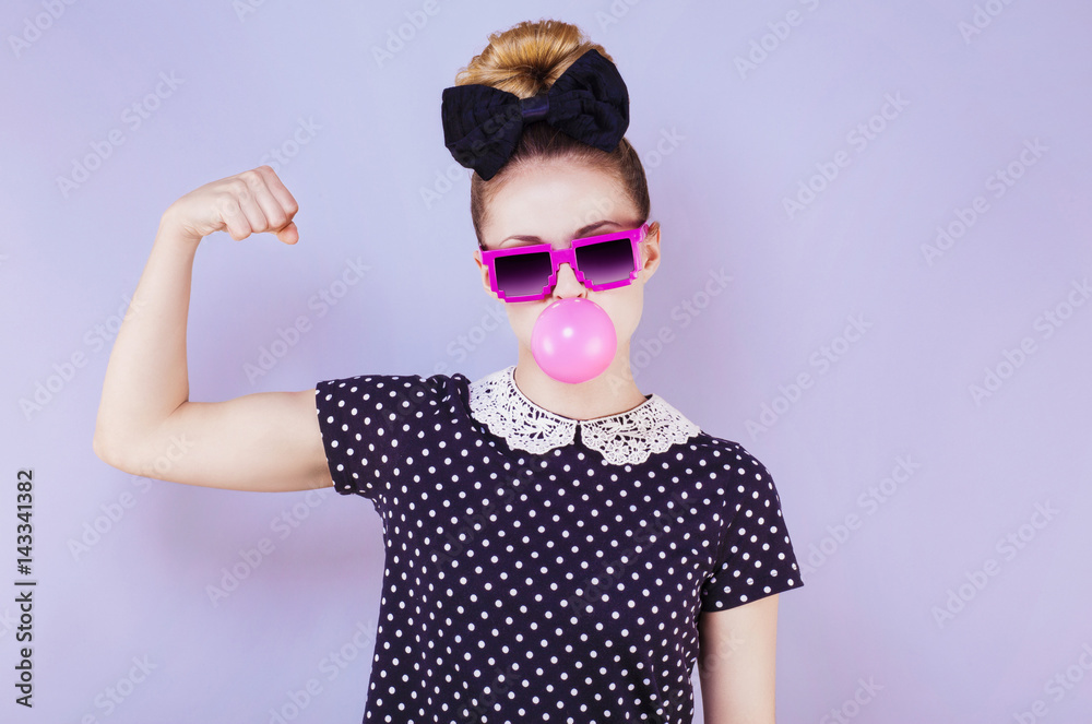Portrait humoristique d'une jeune femme faisant une bulle de chewing gum en montrant son biceps 