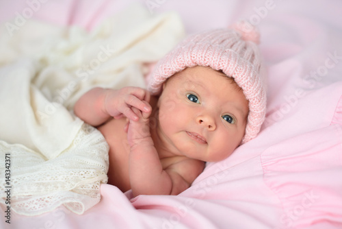 Newborn baby girl in pink knitted hat on pink blanket	