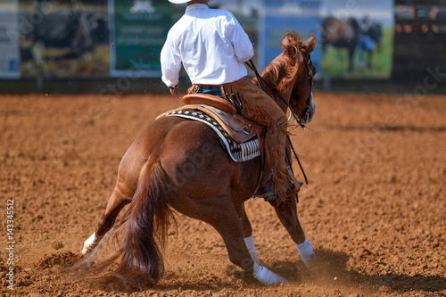 A rear view of western rider sliding the horse in the dirt