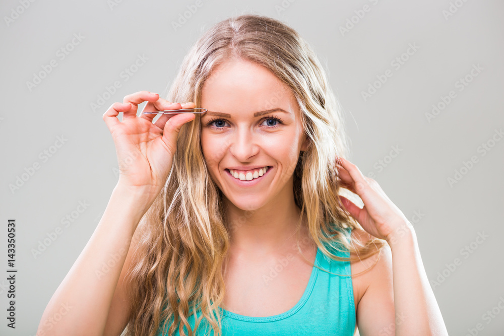 Beautiful young woman plucking eyebrows on gray background. Beautiful young woman plucking eyebrows on gray background.