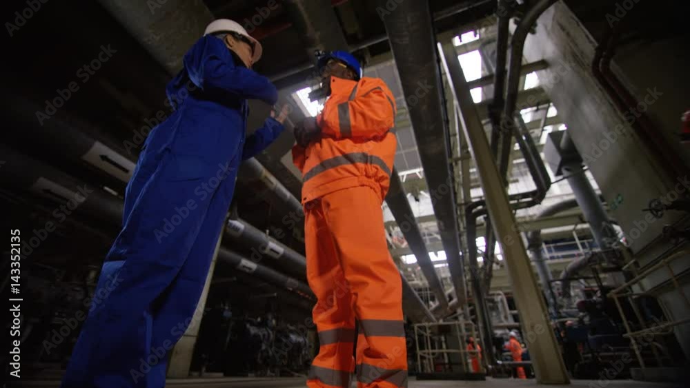 Low angle view male & female engineers in power station discussing operations Low angle view male & female engineers in power station discussing operations