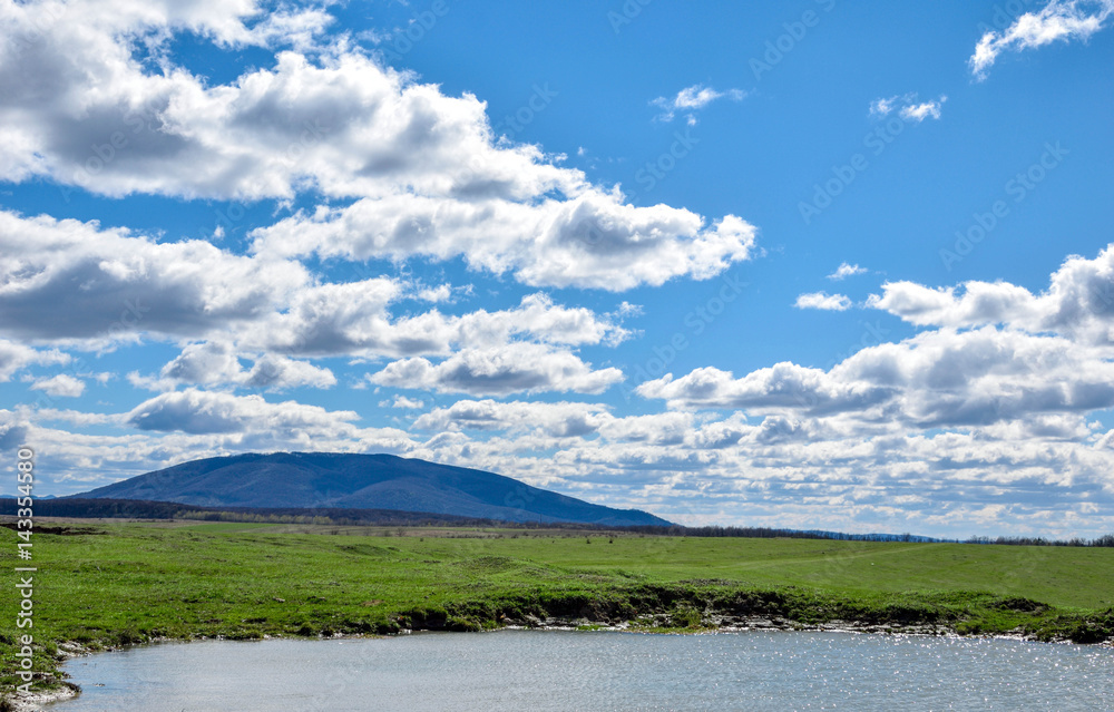 Fototapeta premium beautiful blue sky with white clouds. a beautiful green meadow with a small lake and beautiful mountain