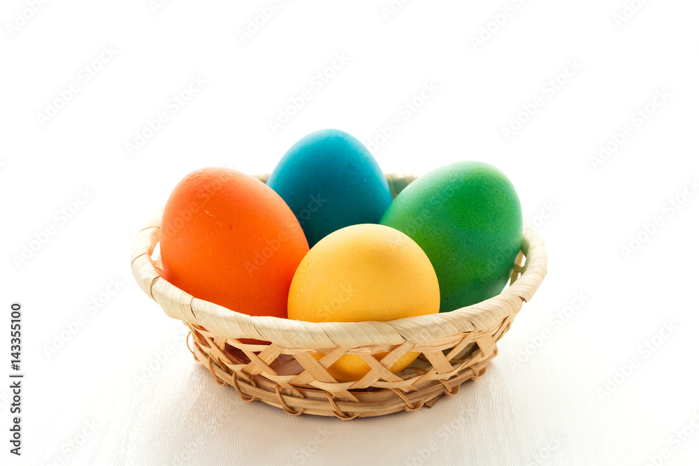 Multicolored easter eggs in a basket, on a white wooden background. The concept of a holiday and a happy Easter. With space for text