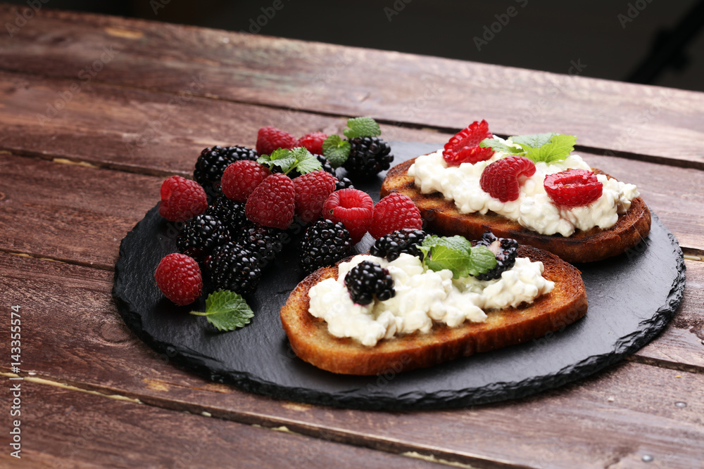 Bread with cheese cream and blackberries and raspberries for lunch table. Sharing antipasti on party or summer picnic time over wooden rustic background. Bread with cheese cream and blackberries and raspberries for lunch table. Sharing antipasti on party or summer picnic time over wooden rustic background.