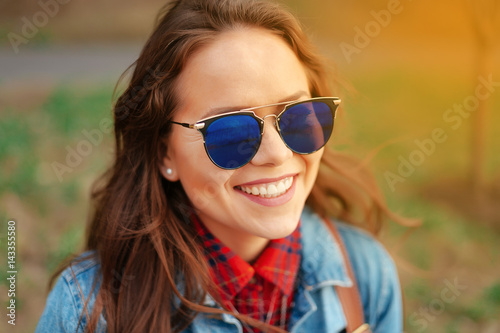 Happy girl with sunglasses smiling and looking at the camera at sunset