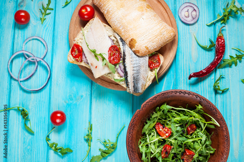 sandwiches with herring and salad with arugula on blue wooden table sandwiches with herring and salad with arugula on blue wooden table
