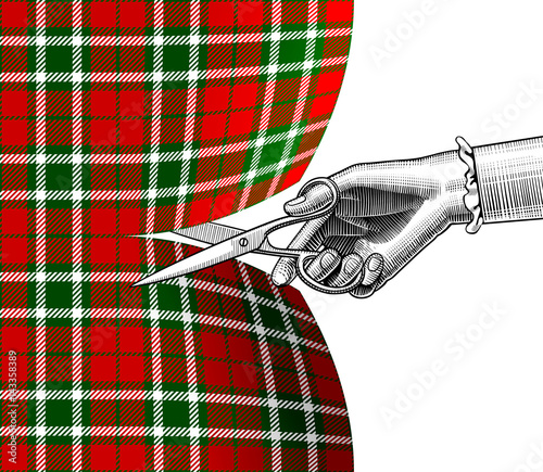 Woman's hand with scissors cutting tartan fabric