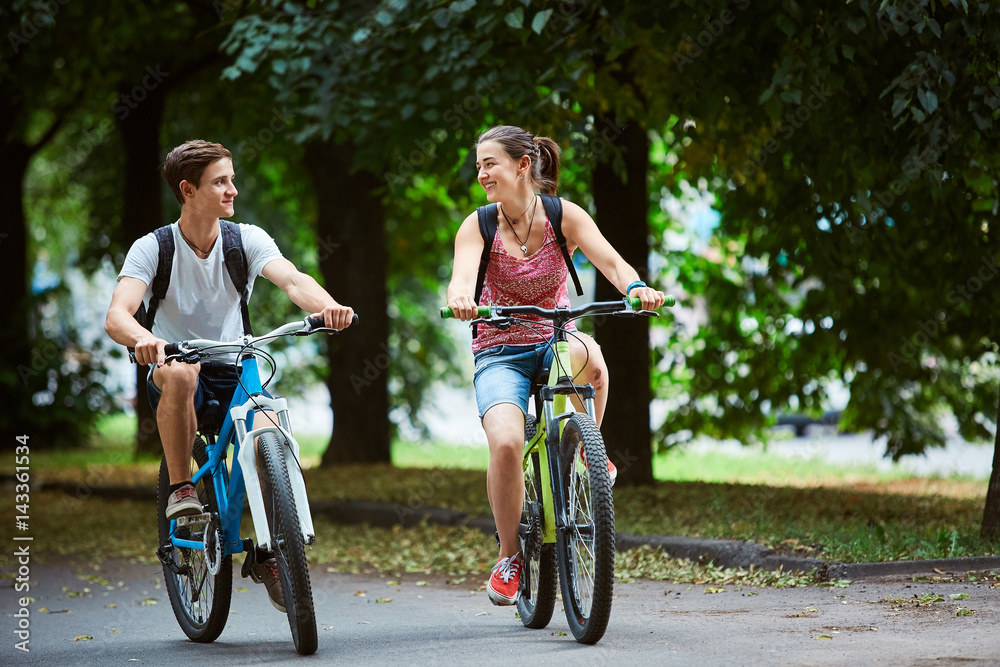 Young people, couple with bicycles in the park. A loving couple on a date on a summer evening. The guy with the girl hugs and kisses. Youth, first feelings, first love, first dates Young people, couple with bicycles in the park. A loving couple on a date on a summer evening. The guy with the girl hugs and kisses. Youth, first feelings, first love, first dates