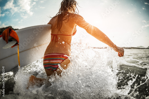 Canvas Print Woman runs into the ocean with surfboard and lots of splashes