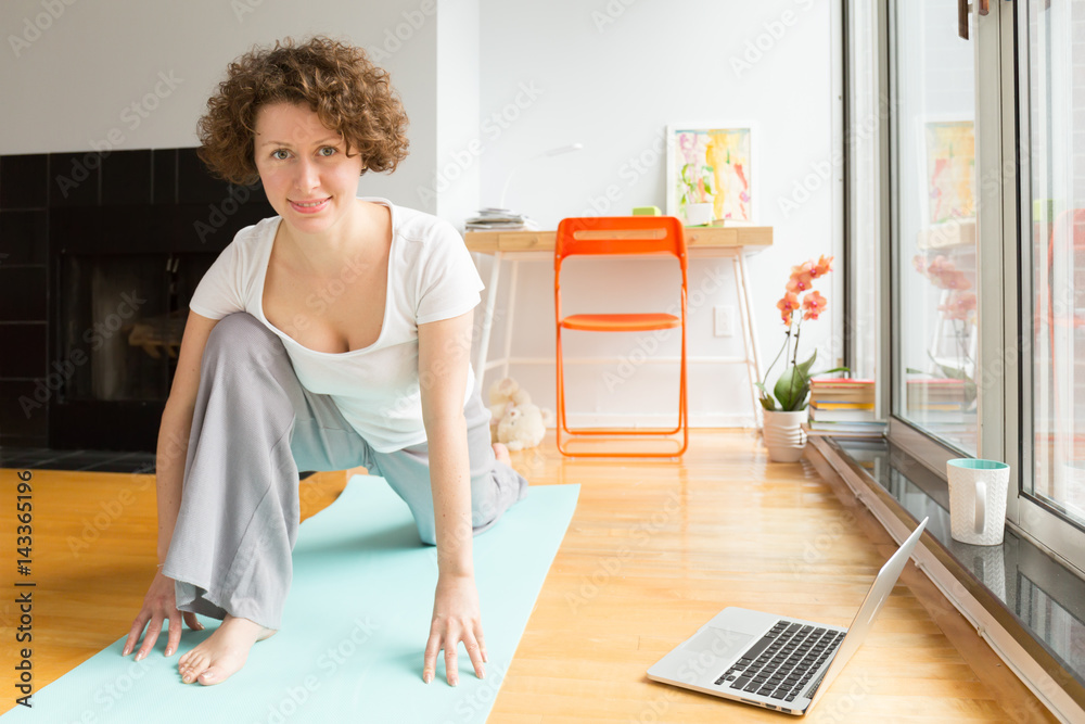 Woman doing yoga with online app on computer in her living room Woman doing yoga with online app on computer in her living room