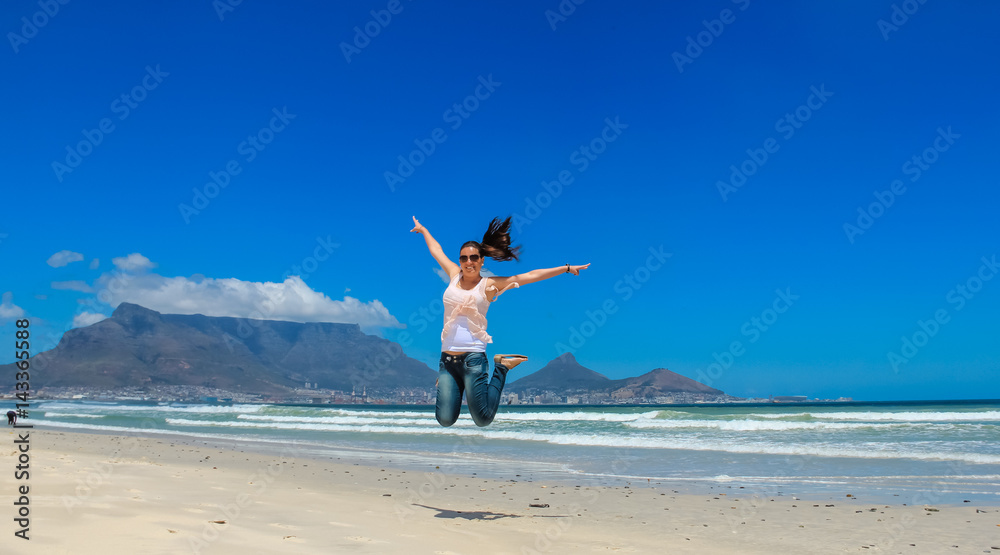Beautiful girl jumping at Milnerton beach, Cape Town. Table Mountain and breaking waves in the background. Concept photo of happiness, freedom and lifestyle. Beautiful girl jumping at Milnerton beach, Cape Town. Table Mountain and breaking waves in the background. Concept photo of happiness, freedom and lifestyle.