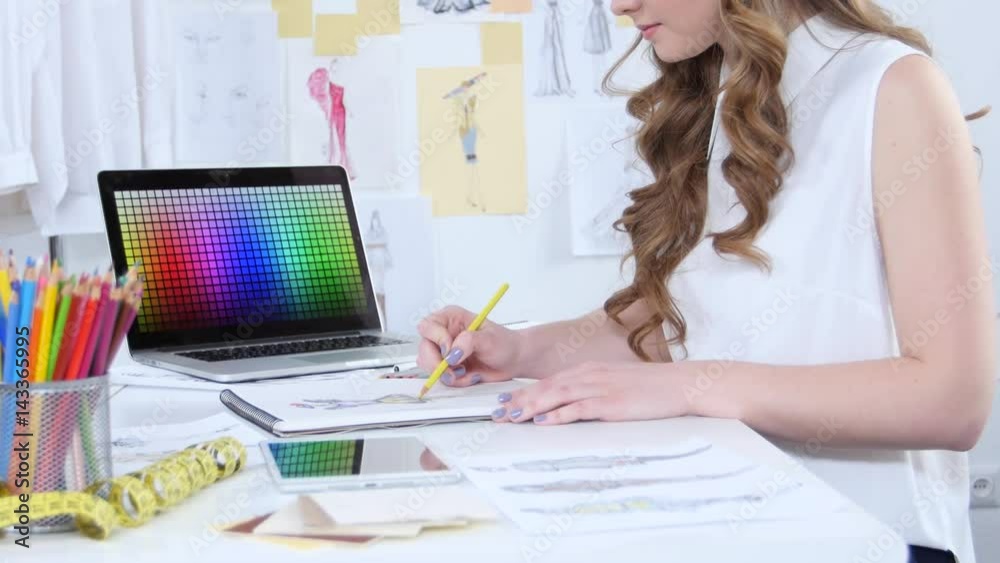 Fashion designer draws sketches for a new collection and looks at the computer Fashion designer draws sketches for a new collection and looks at the computer