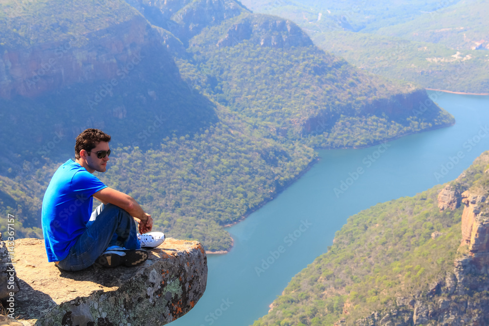 Young man sitting on stone on the cliff in the Blyde River Canyon, South Africa