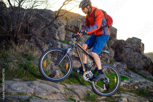 Cyclist Riding Mountain Bike Up Rocky Hill on the Spring Trail at Sunset. Extreme Sports Concept.