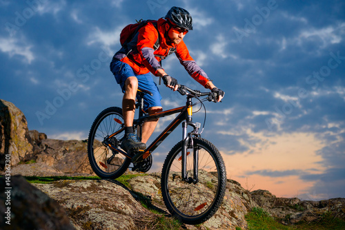 Cyclist Riding Mountain Bike Down Spring Rocky Hill at Beautiful Sunset. Extreme Sports and Adventure Concept.