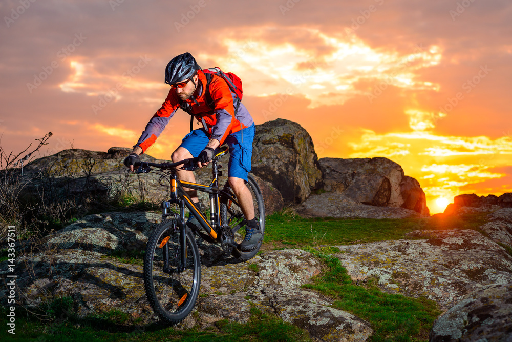 Cyclist Riding Mountain Bike Down Spring Rocky Hill at Beautiful Sunset. Extreme Sports and Adventure Concept.