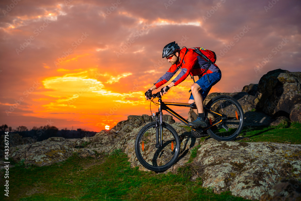 Cyclist Riding Mountain Bike Down Spring Rocky Hill at Beautiful Sunset. Extreme Sports and Adventure Concept. Cyclist Riding Mountain Bike Down Spring Rocky Hill at Beautiful Sunset. Extreme Sports and Adventure Concept.