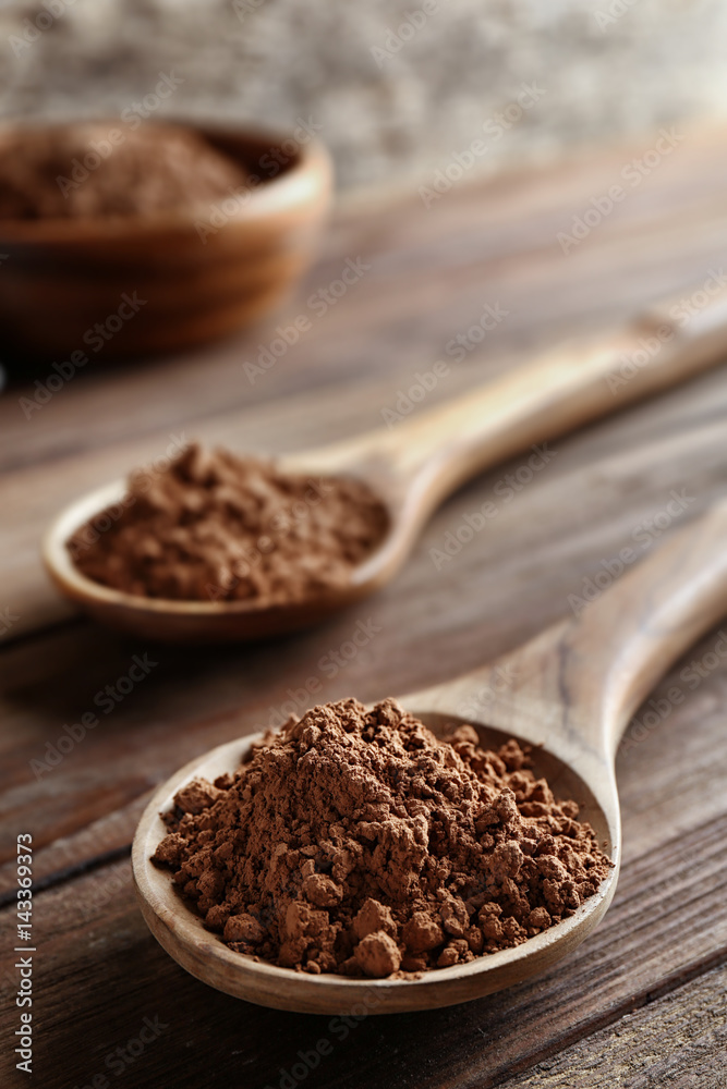 Two spoons with cocoa powder on wooden table