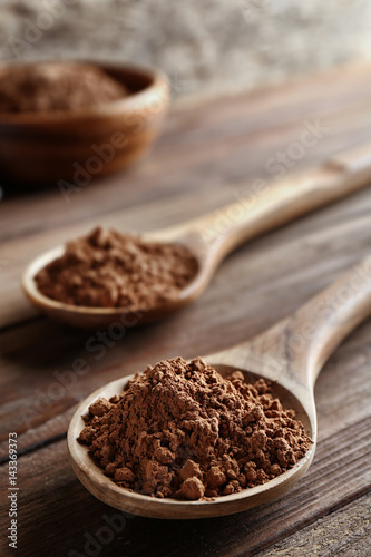 Two spoons with cocoa powder on wooden table