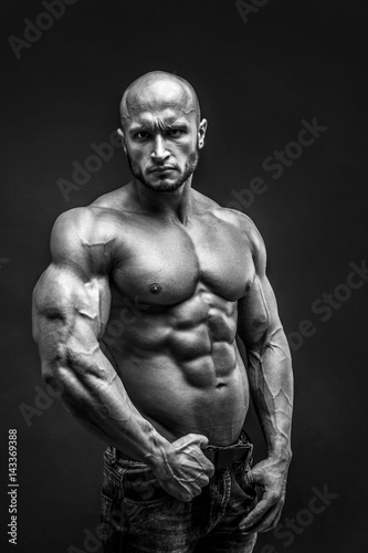 Shirtless muscled fitness man. Cool looking. Tough guy. Bald. Tanned skin. Studio shot on black background.