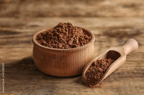 Wooden bowl and scoop with cocoa powder on rustic background