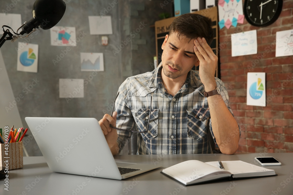 Handsome young man suffering from headache while working in office Handsome young man suffering from headache while working in office