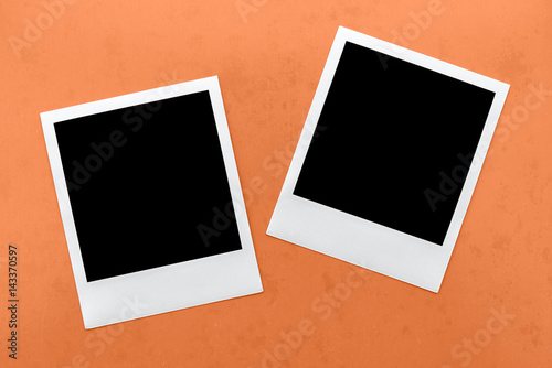 two blank instant camera film frames on orange background.