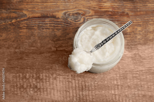 Spoon with coconut oil and jar on wooden background