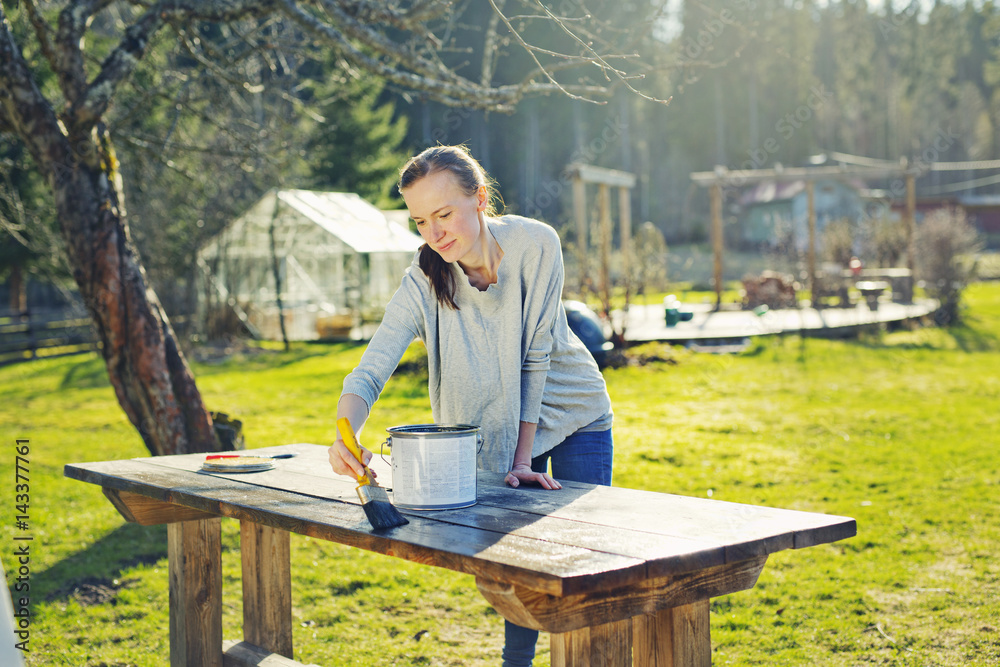 Finland, Paijat-Hame, Heinola, Mid adult woman oiling wooden table in garden Finland, Paijat-Hame, Heinola, Mid adult woman oiling wooden table in garden
