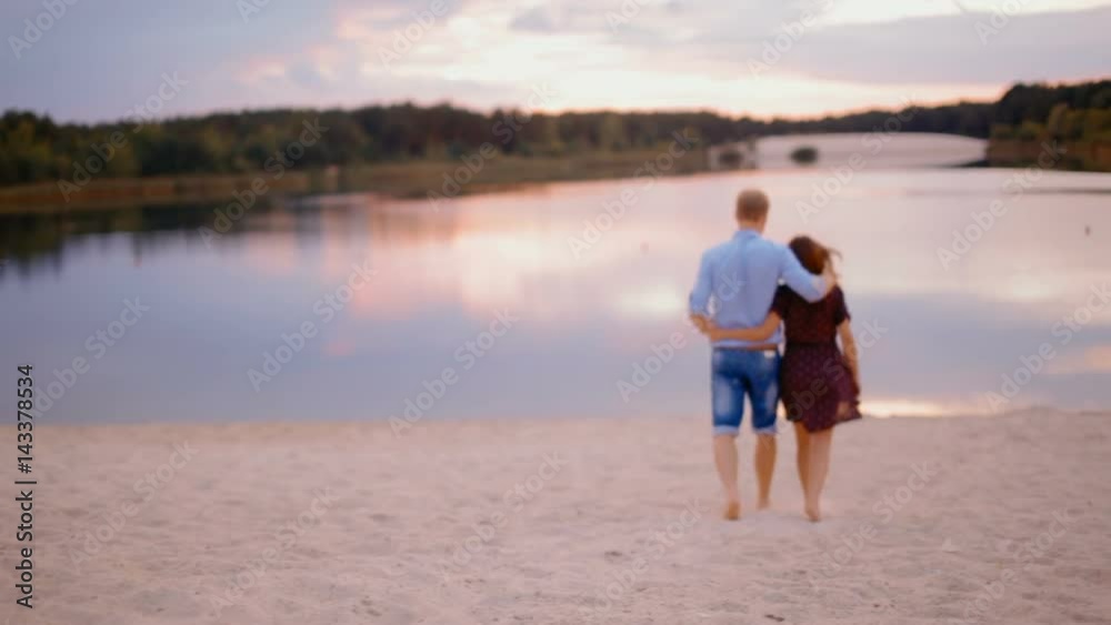 Young Beautiful Couple Running on Sand on the Beach to the Forest to the Picturesque Lake at Sunset and Embraces Young Beautiful Couple Running on Sand on the Beach to the Forest to the Picturesque Lake at Sunset and Embraces