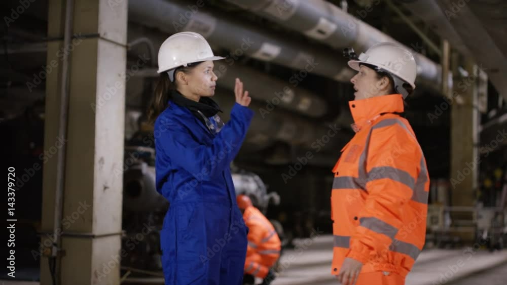 Engineers walking through power plant with other workers in background Engineers walking through power plant with other workers in background