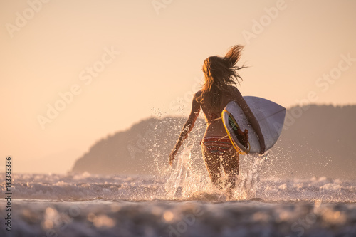 Canvas Print Woman runs into the ocean with surfboard